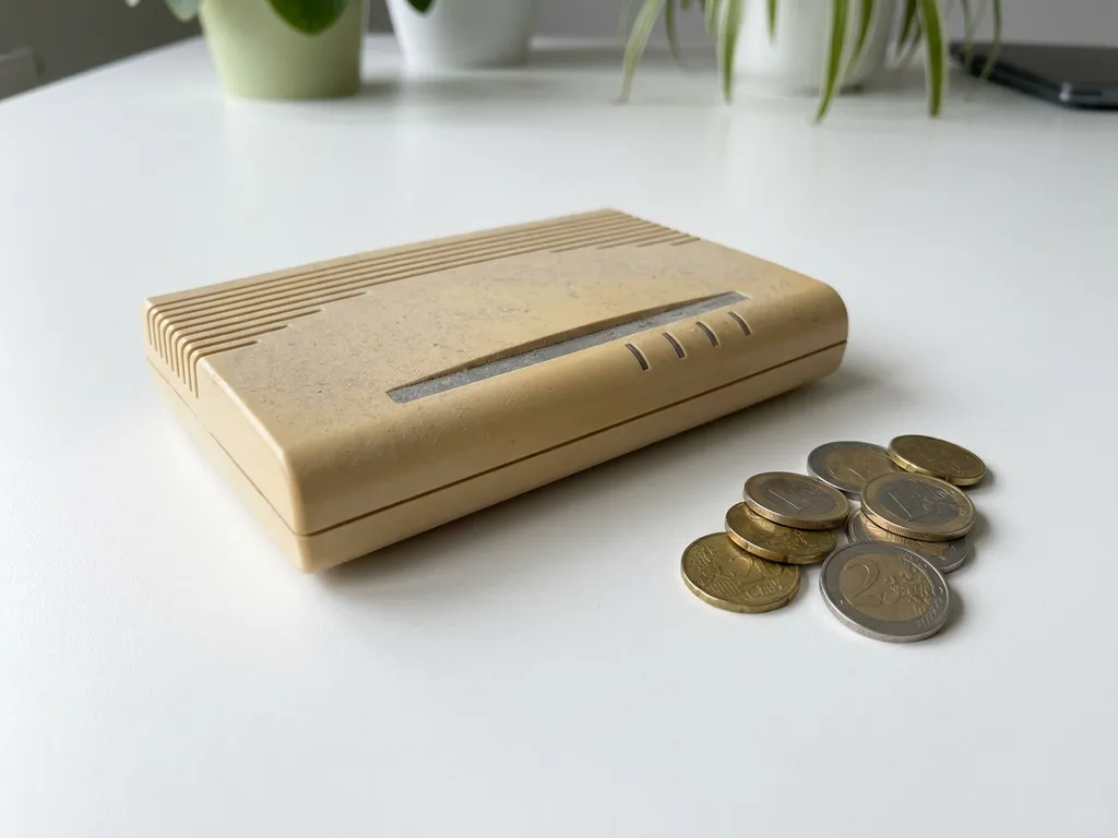Verouderde beige router uit de jaren 2000 naast een stapeltje euromunten op een wit oppervlak.